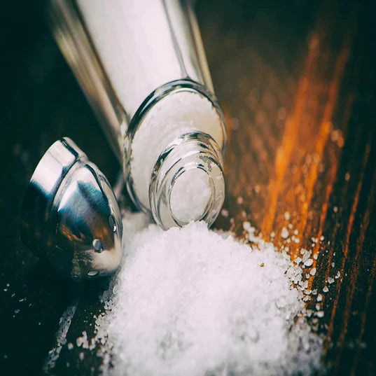 glass salt shaker with top off spilling salt onto wooden surface