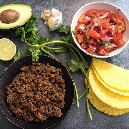big black bowl filled with vegetarian taco meat substitute next to taco shells avocado salsa cilantro garlic and a lime