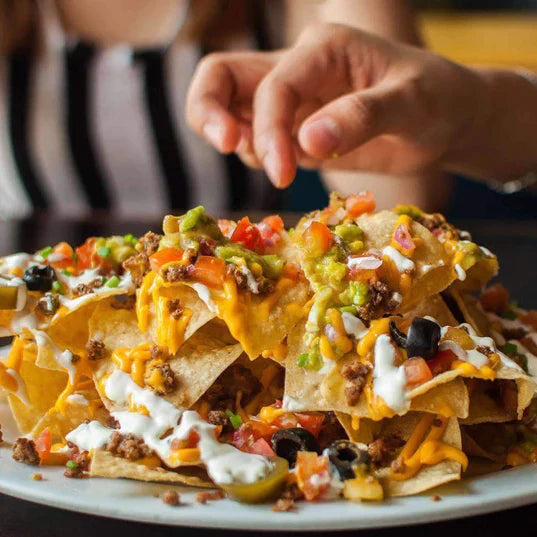 vegetarian taco meat substitute featured on big plate of nachos topped with olives tomatoes avocado green peppers and cheese