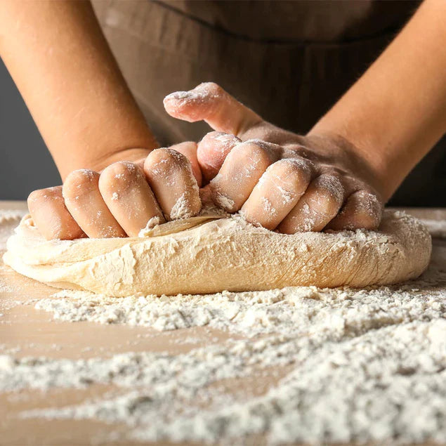 who hand needing dough in flour on wooden surface