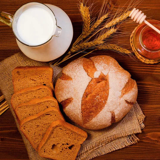 whole loaf of honey wheat bread along side of sliced honey wheat bread milk and honey in glass jar