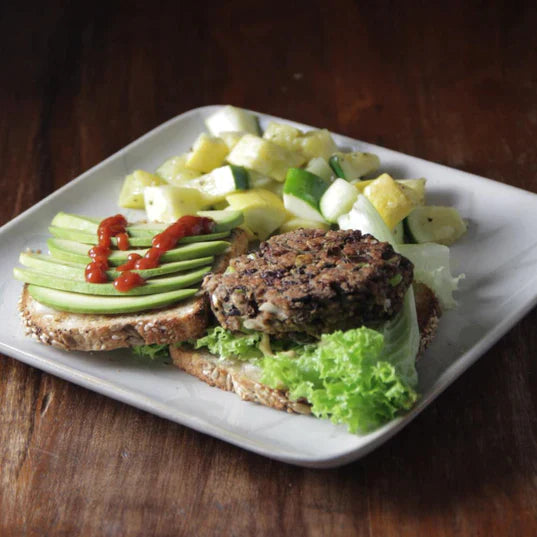black bean burger patty on whole grain bread with avocado ketchup lettuce and a side of vegetables