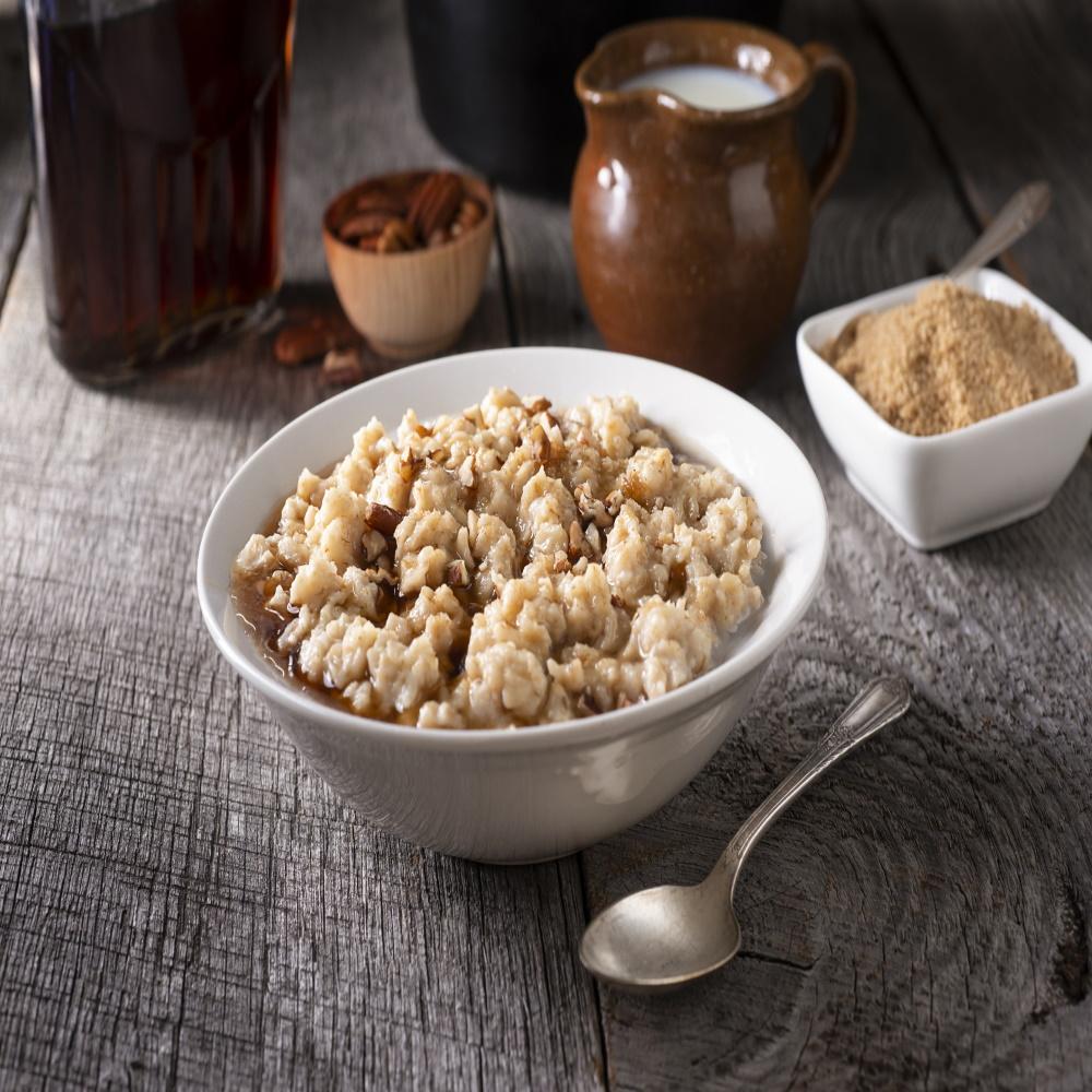 maple grov oatmeal with maple syrup on top in white bowl with silver spoon on the side and sugar cream nuts and syrup in the background