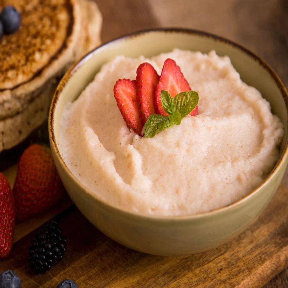 strawberry flavored creamy wheat with strawberries on top in green ceramic bowl with pancakes and fruit on the side