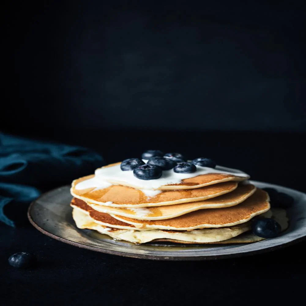 stack of ready hour pancakes with blueberries and melted butter on top on blue plate