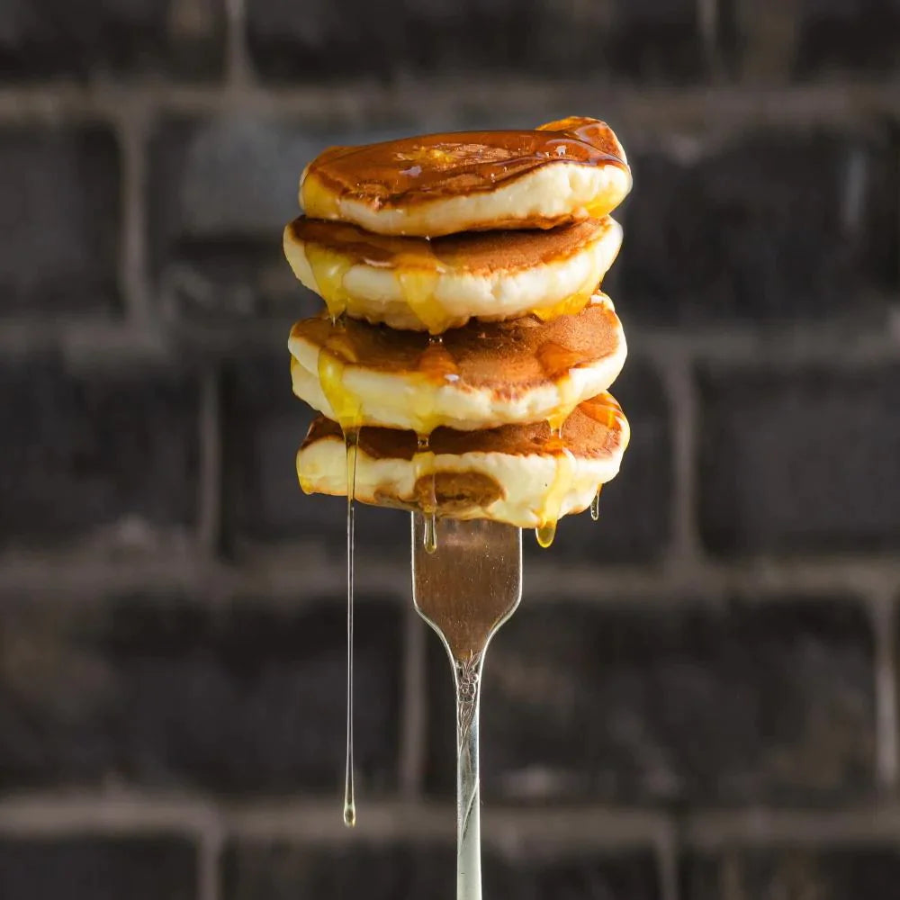 four stacked mini pancakes stuck on fork with syrup dripping down pancakes
