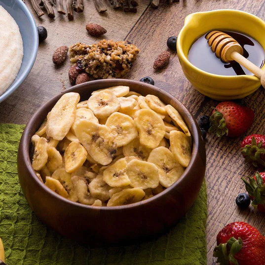 banana chips in wooden bowl with strawberries honey and nuts around bowl