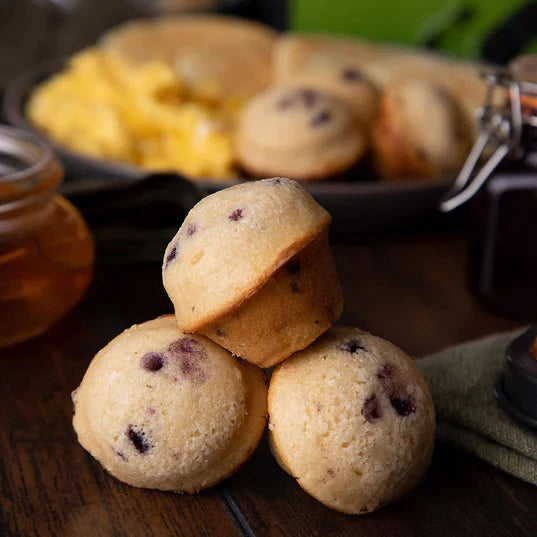 three breakfast muffins with full plate of breakfast foods behind them and honey on the side