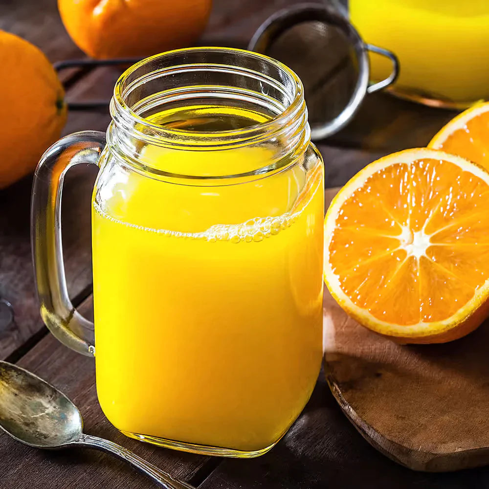 orange energy drink in glass with handle and silver spoon on left side with oranges in background