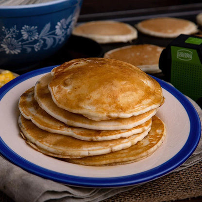 stack of four buttermilk pancakes on white and blue plate with cooking pancakes in the background