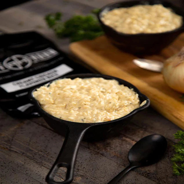 creamy chicken flavored rice in black skillet with packaging and black spoon on either side