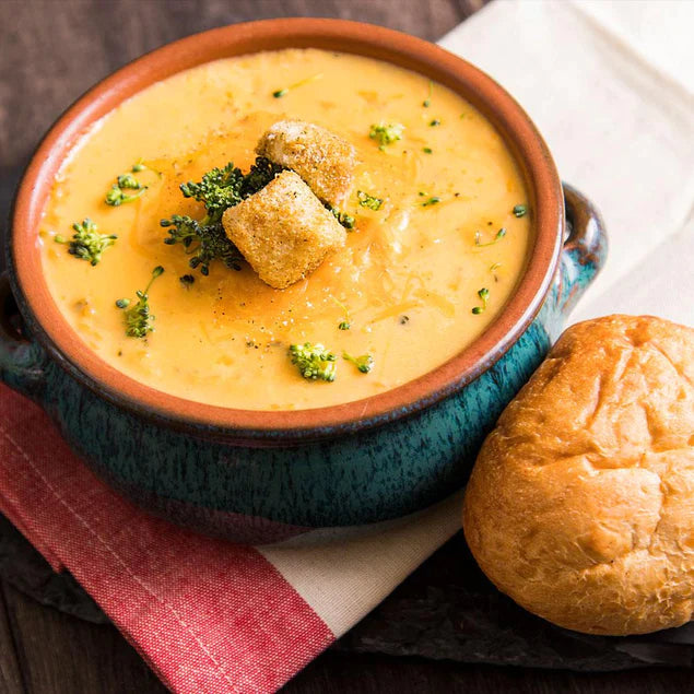 cheesy broccoli soup with croutons on top in blue and orange bowl with bread at side